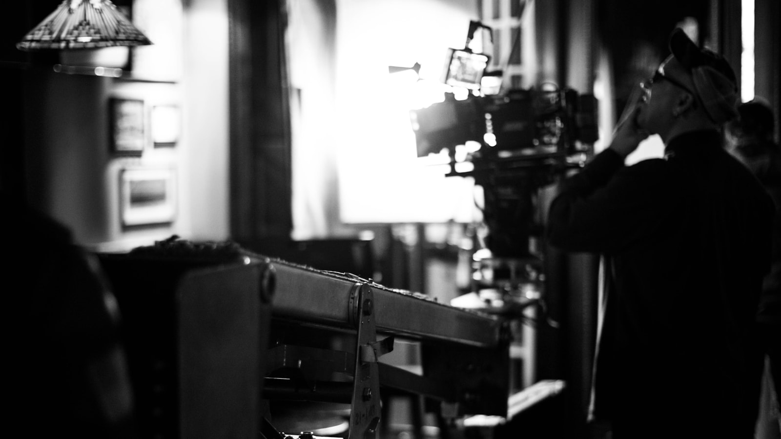 Black and white film still of a director lining up a shot on a cinema camera in a dark set